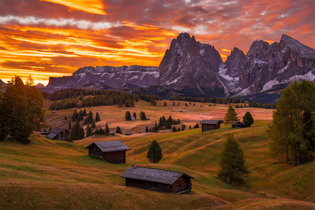 Sunrise over Alpe di Siusi with fall-colored meadows, alpine huts, and the Sciliar peaks in the Dolomites