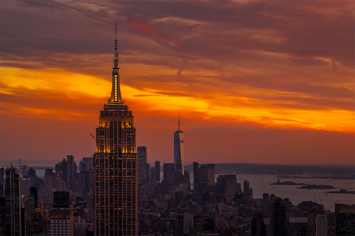 Empire State Building illuminated at sunset with the Manhattan skyline and harbor in the distance