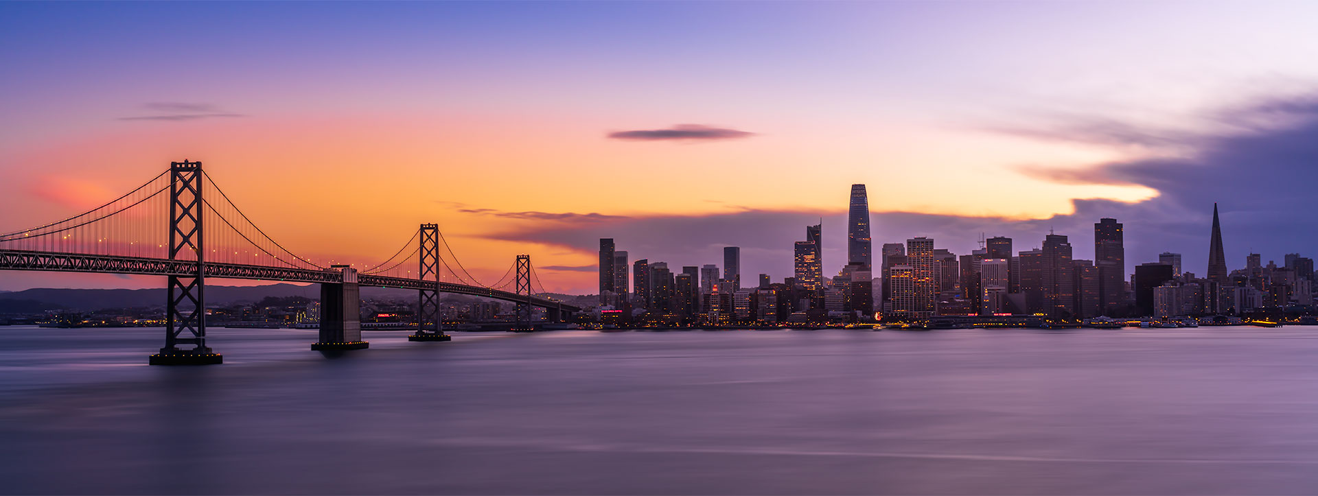 San Francisco skyline at blue hour with the Bay Bridge and calm water