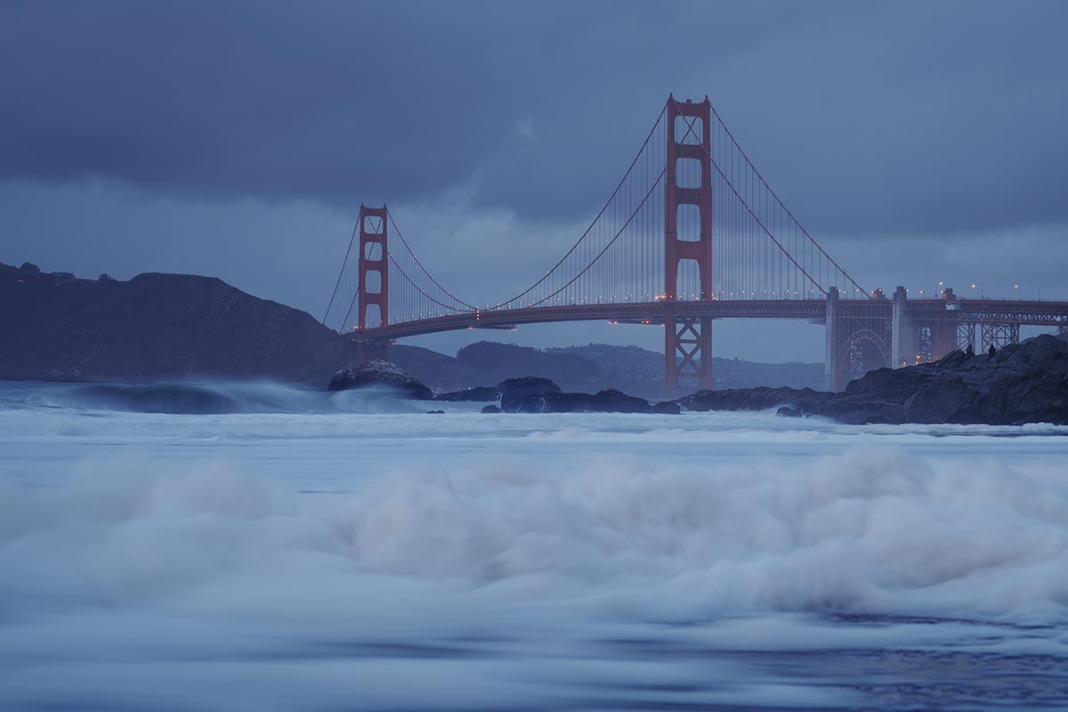 Golden Gate Bridge in soft evening mist with rolling waves at Baker Beach, San Francisco